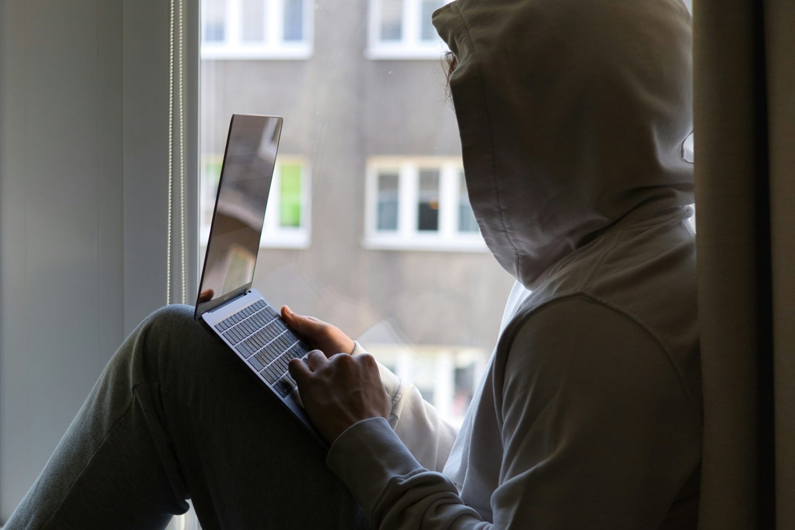 a person sitting on a window sill using a laptop