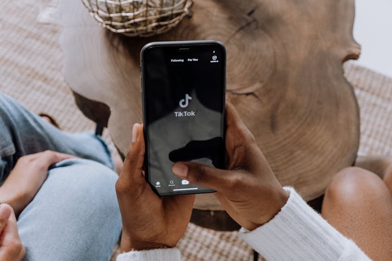 Close-up of hands holding a smartphone displaying the TikTok app interface on a wooden surface.